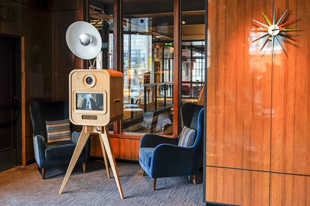 MooMuu Luxury Oak Booth positioned between blue velvet armchairs in an elegant venue.