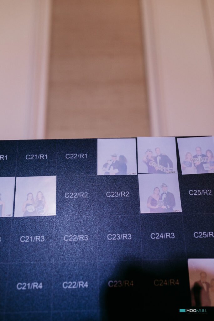 A close-up of a black grid with labelled boxes, some featuring small, slightly blurry premium photo booth hire images of people posing with props. The background is out of focus, showing vertical beige and white panels.