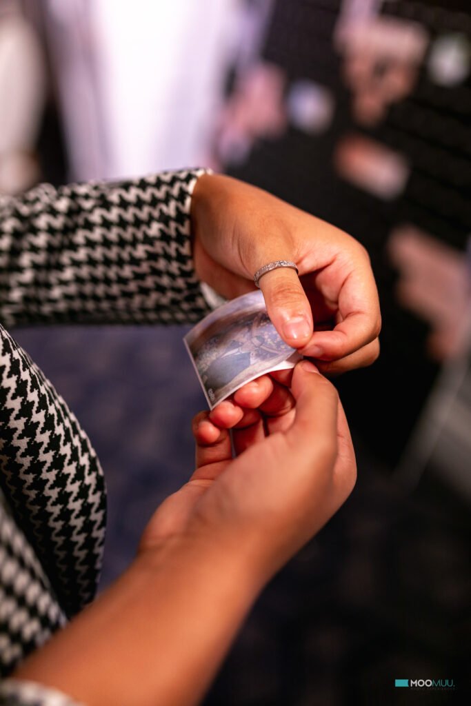 A person in a patterned jacket holds a small photo print from a premium photo booth hire, focusing on the picture. The background is blurred, drawing attention to their hands and the photo.