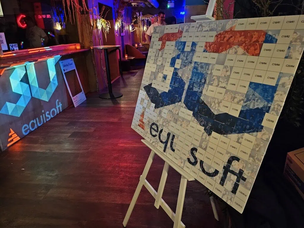 A mosaic board on an easel displays the word "equisoft" in blue, red, and orange tiles. In the background, a bar counter with an illuminated "equisoft" logo and neon lights sets a vibrant scene for a corporate event experiential or graffiti wall hire.