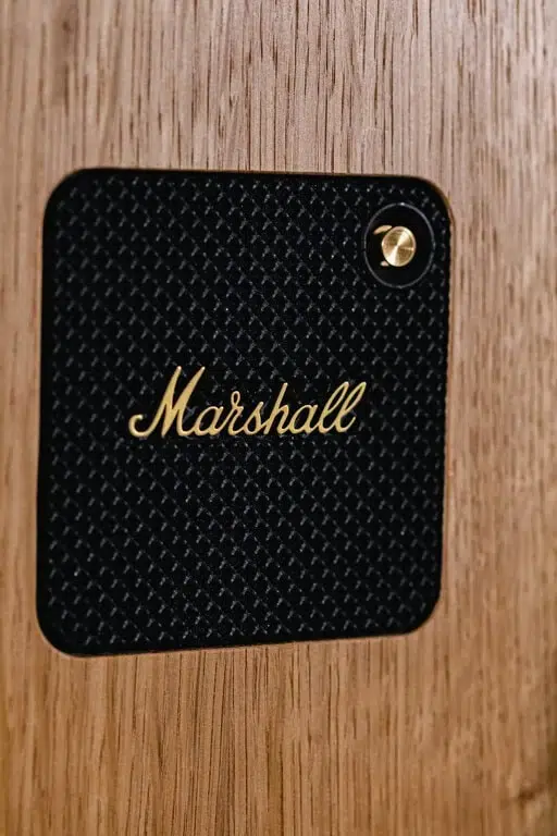 Close-up of a black, textured panel with the gold "Marshall" logo and a gold screw in the upper right corner, mounted on a light brown wood surface—perfect for adding style to premium photo booth hire or graffiti wall hire events.