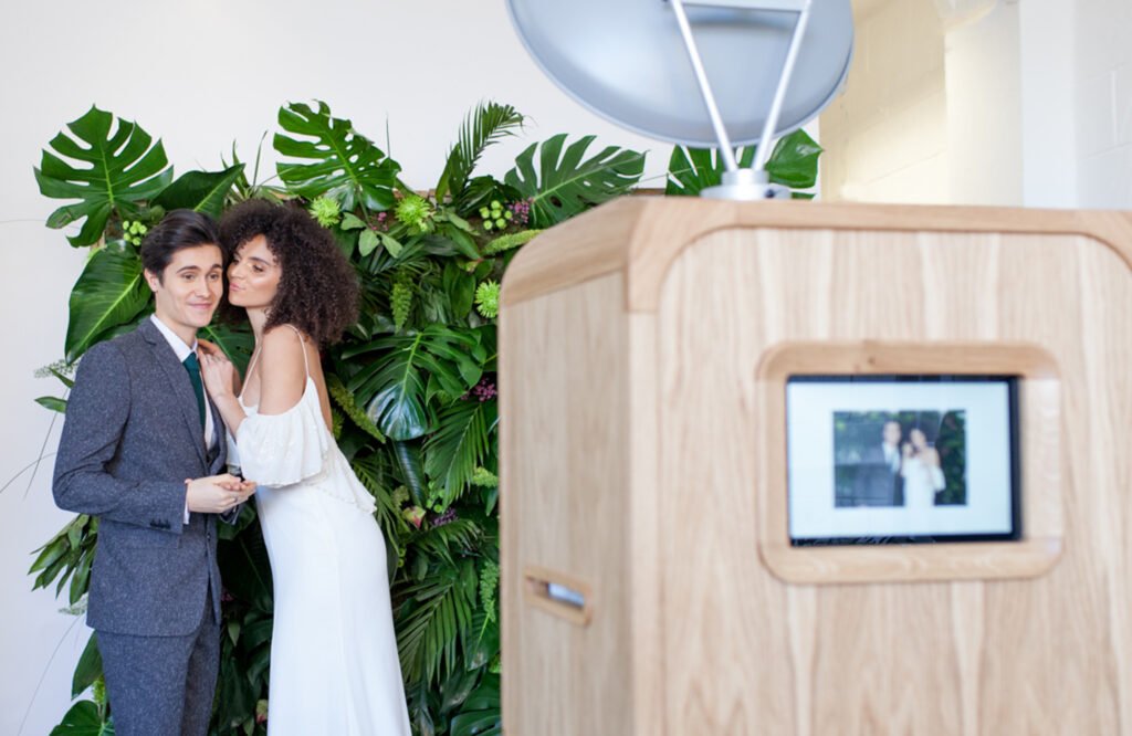 Wedding couple posing in front of a foliage backdrop with their portrait displayed on the Luxury Oak Booth.