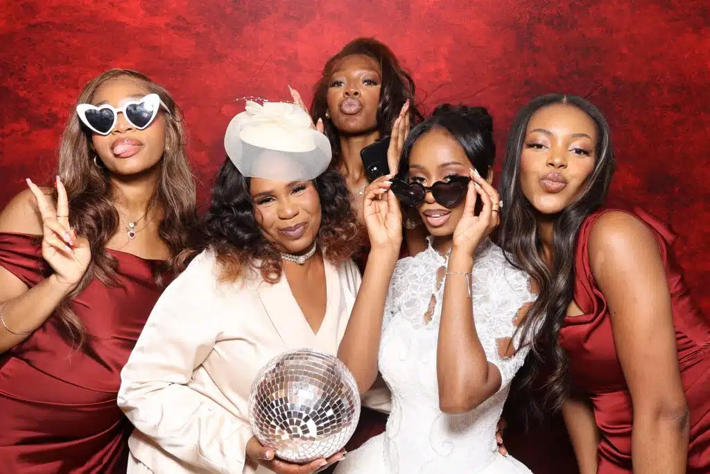 Five guests enjoying a MooMuu photo booth session against a red backdrop.