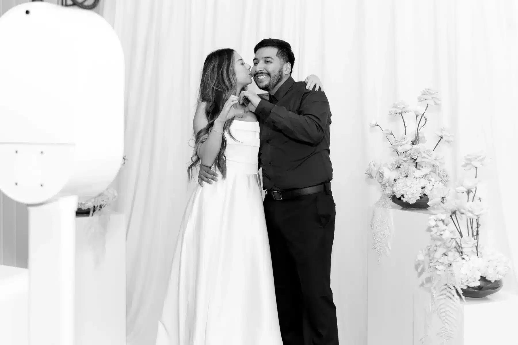 Black-and-white wedding portrait beside an elegant white photo booth